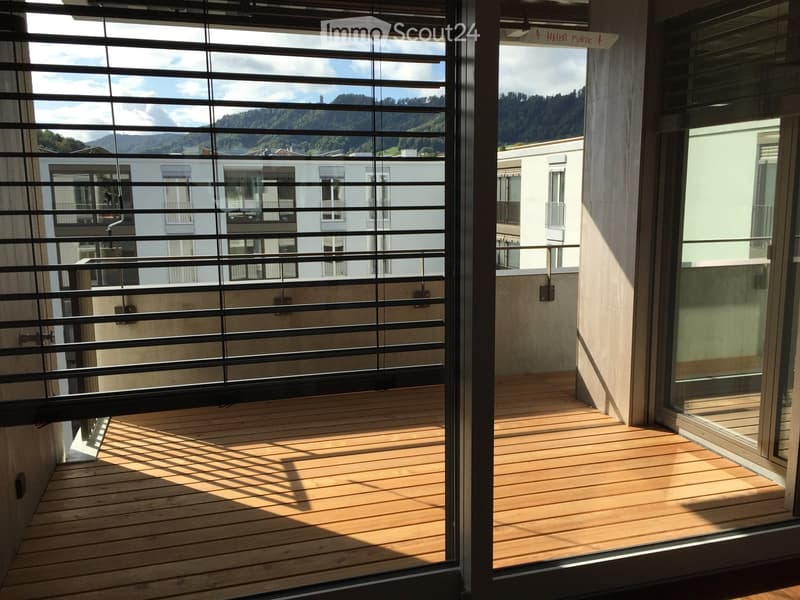 Balcony with wooden decking, metal railings, and a view of a cityscape and mountains.