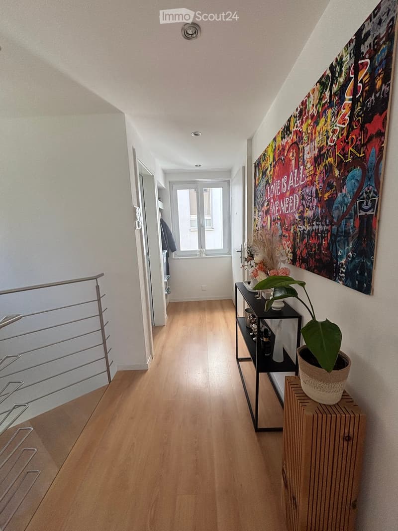 Hallway with wooden flooring, a black side table with a potted plant, and a colorful wall art piece.