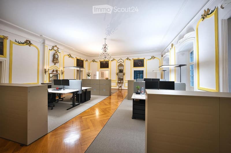 Elegant office space with wooden flooring, ornate mirrors, chandeliers, desks, chairs, computer monitors, cabinets, and lamps.