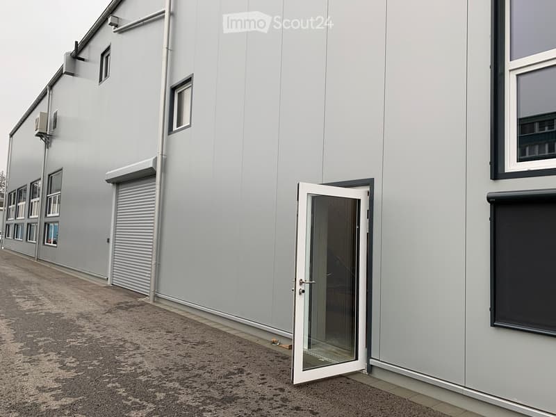 Modern grey building with multiple windows, a large roller shutter, and an open glass door leading to the interior.