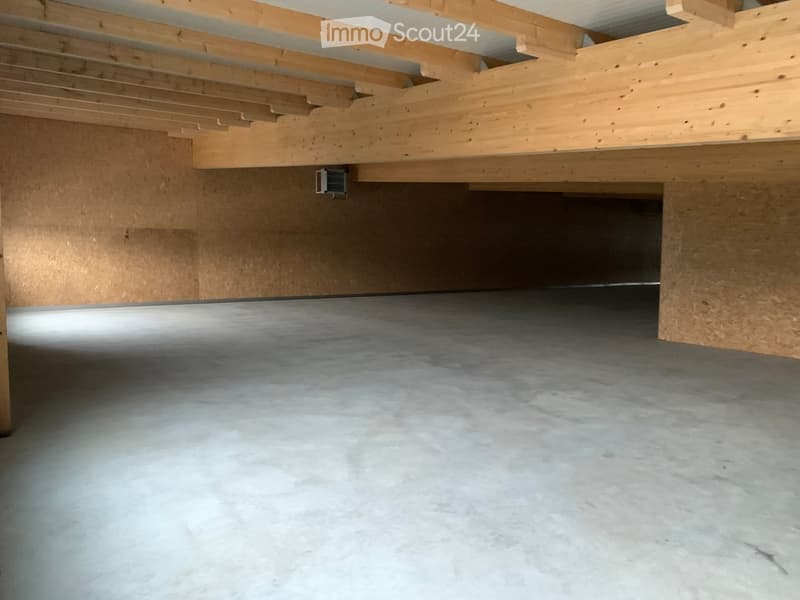 Empty garage with concrete floor, wooden ceiling beams, and exposed wooden walls.