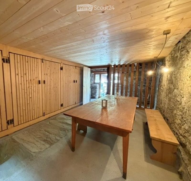 A rustic wooden room with a long wooden table, a bench, and wooden cabinets. The walls are made of stone, and the ceiling is wooden.