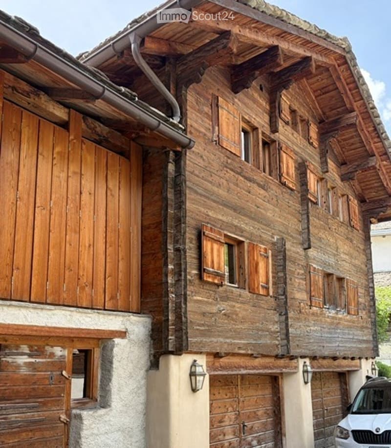 Traditional wooden chalet with multiple windows, wooden shutters, and a garage entrance.