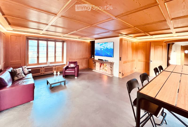 wooden paneled walls, fireplace, flat screen TV, couch, table, side table, chairs, windows, radiator