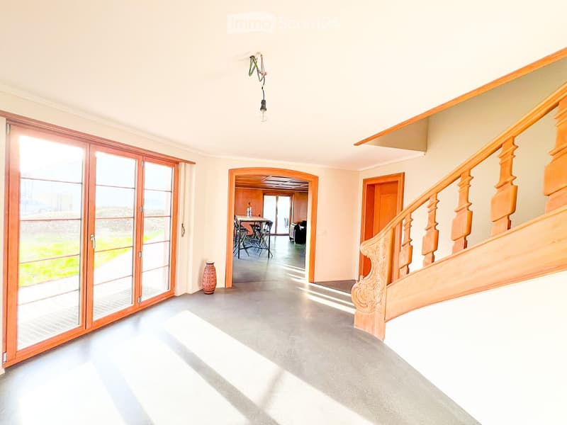 Open hallway with sliding glass doors, wooden staircase, gray floor, vase, table with chairs, white walls