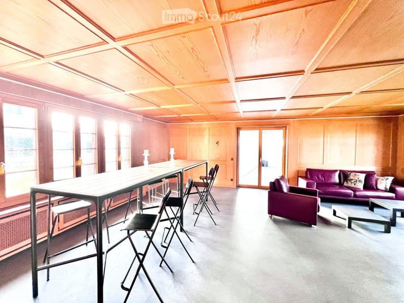 large room, long table with barstools, purple couch, glass windows, wooden wall paneling, ceiling light