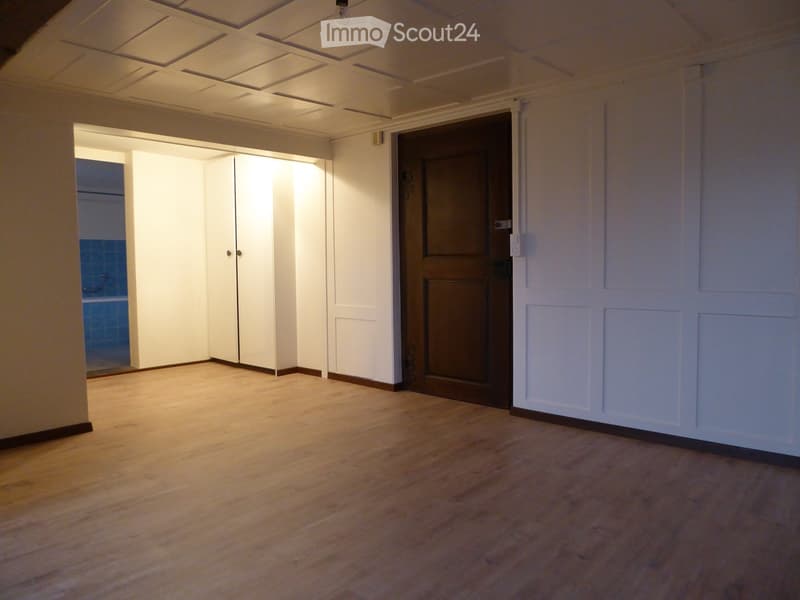 Empty room with wooden flooring, white walls, and a closed wooden door leading to another room.