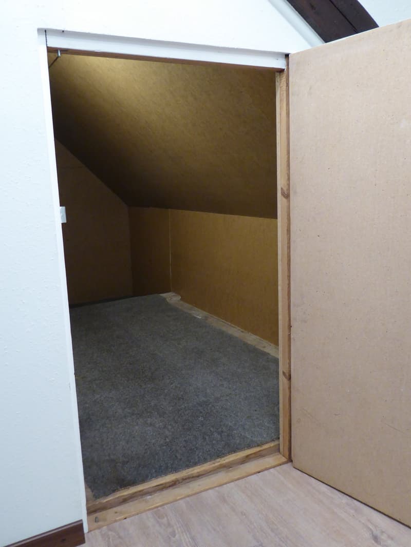Empty room with wooden flooring and carpeted area, featuring an open doorway with visible wooden frame and white trim.