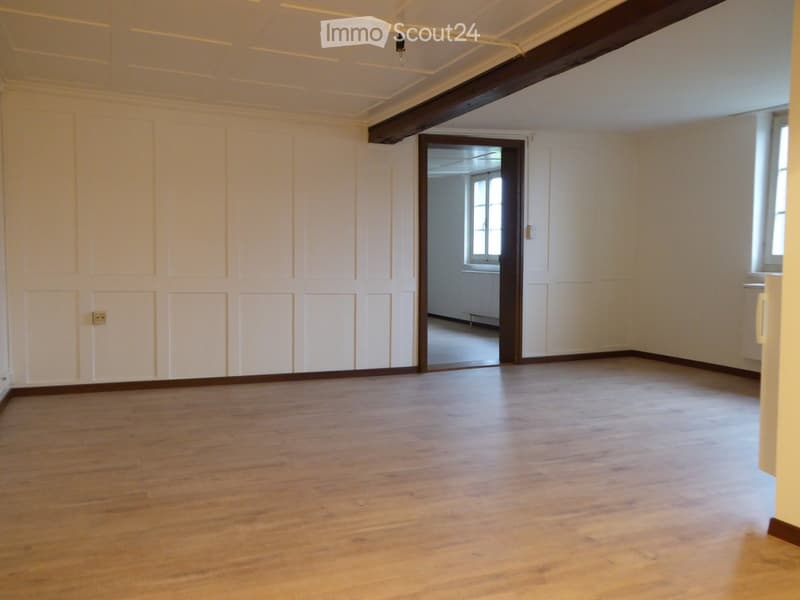 Empty room with wooden flooring, white walls, and a visible doorway leading to another room.