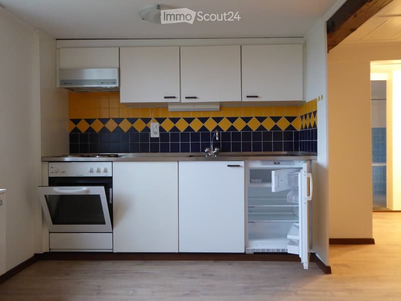 Compact kitchen with white cabinets, stainless steel appliances, and a colorful backsplash featuring yellow and blue tiles.
