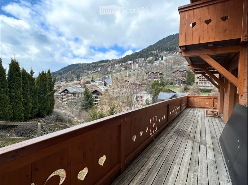 wooden balcony with heart shaped cutouts, wooden railing, wooden floor, view of mountains and village