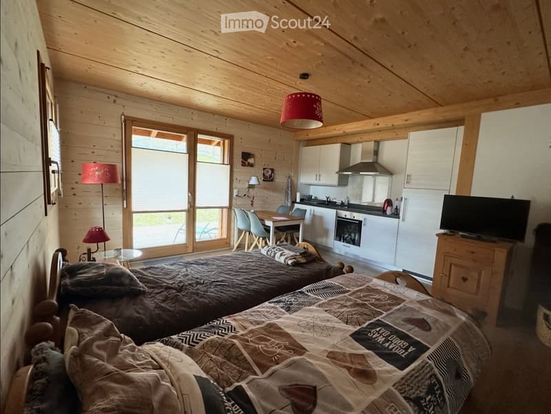 Bedroom with two beds, wooden ceiling, wooden floor, kitchen with dining table, white cabinets, stove, oven, microwave, refrigerator, TV, lamps, and a glass door leading to a patio.