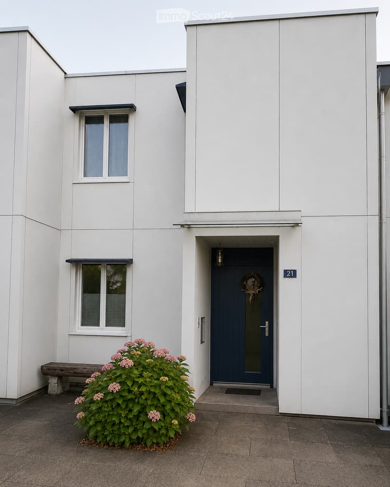 Modern white building exterior with a blue front door, decorative wreath, and small garden with pink flowers and a wooden bench.