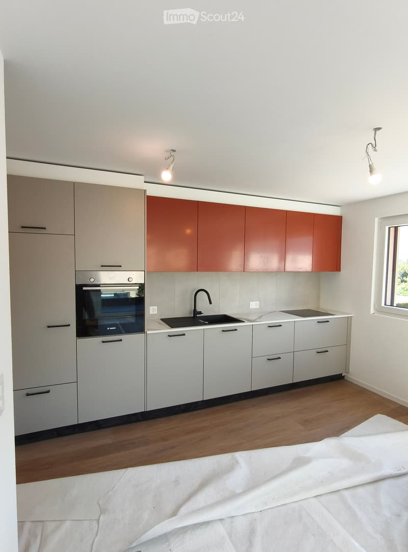 Modern kitchen with white and brown cabinets, stainless steel oven, sink, and faucet, wooden flooring, and a large window.