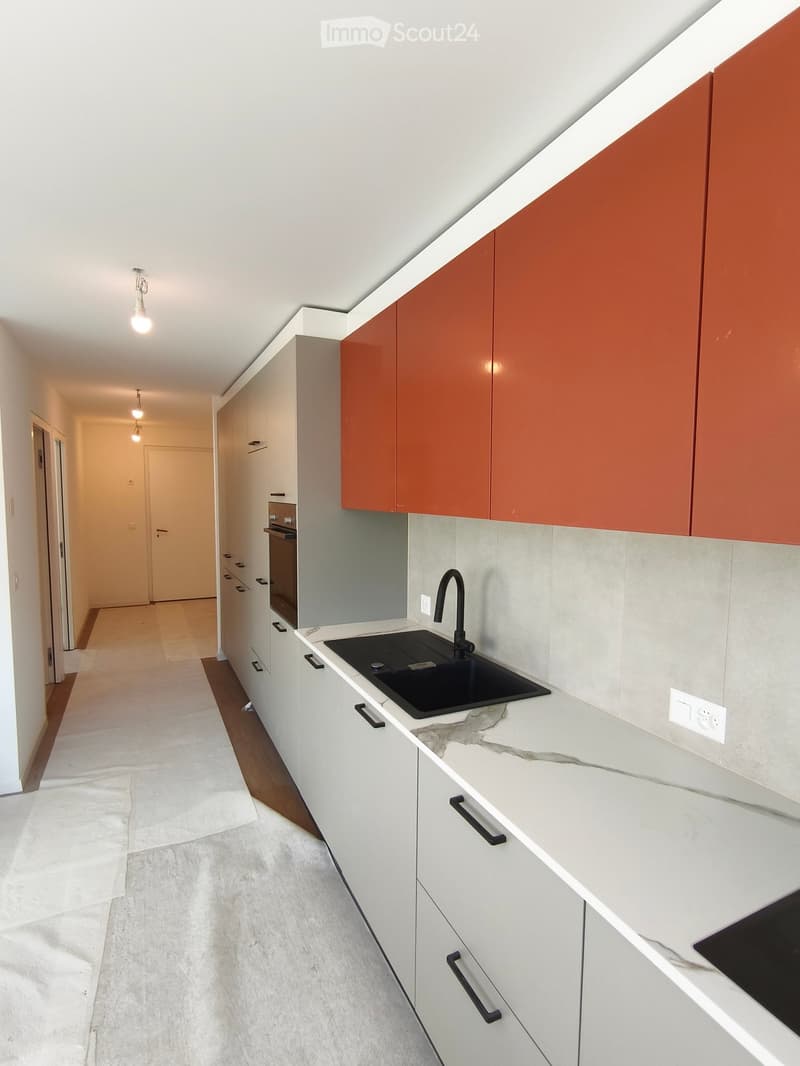 Modern kitchen with white and orange cabinets, marble countertop, black sink, and built-in oven.