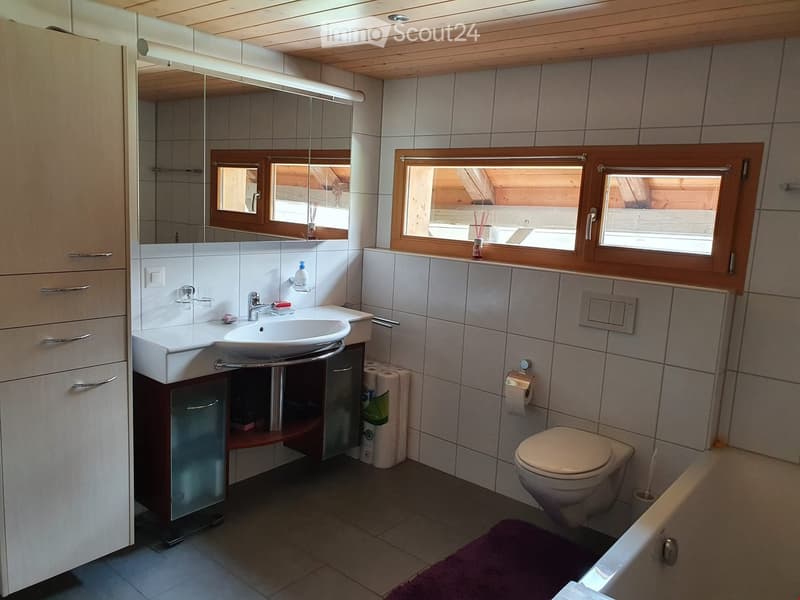 Modern bathroom with a sink, toilet, bathtub, and a large mirror above the sink. The room features wooden windows and a wooden ceiling.