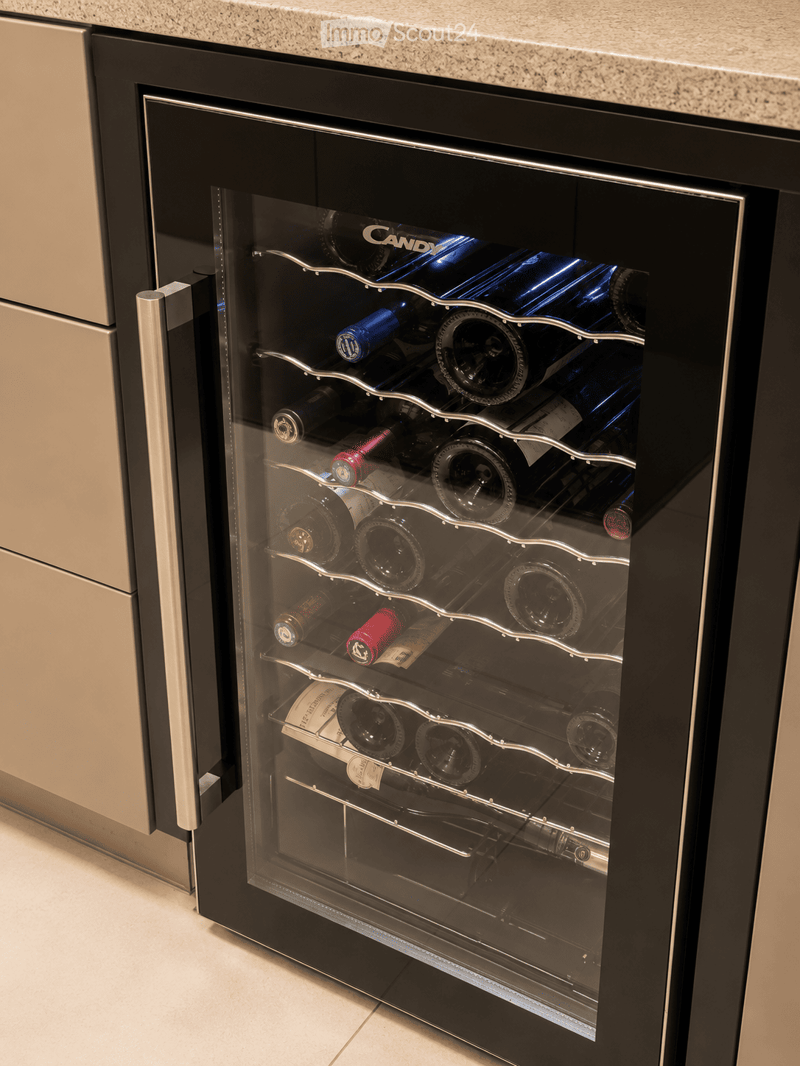 A modern wine cooler with multiple shelves holding various wine bottles, integrated into a sleek kitchen design with a granite countertop and stainless steel accents.
