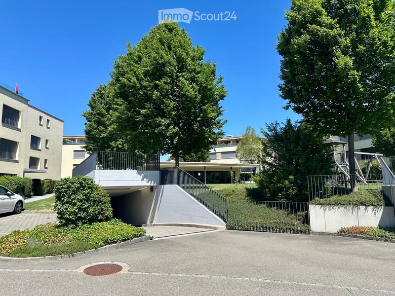 Modern multi-story residential building with a raised ground floor, garage, and landscaped surroundings.