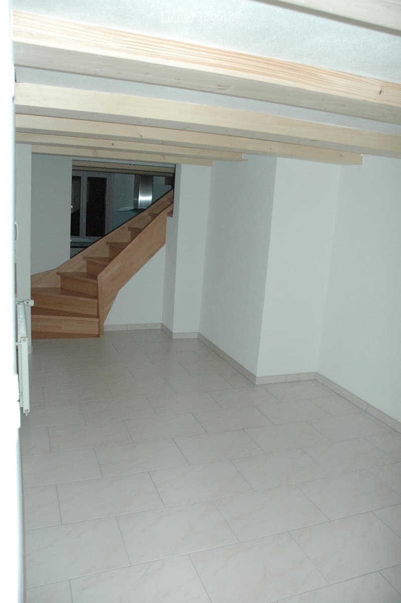 Empty room with tiled floor and light-colored walls, featuring a wooden staircase leading to an adjacent area.