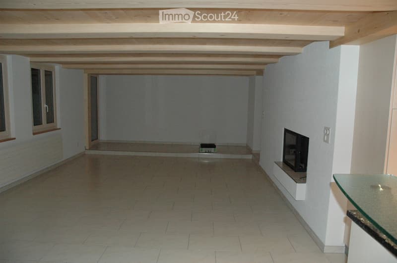 Empty room with tiled floor, white walls, exposed wooden ceiling beams, fireplace, and a small window with a radiator below it.
