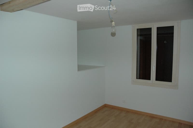 Empty room with light-colored walls, wooden flooring, a single window with white frame, and a built-in shelf on one wall.