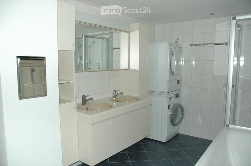 Modern bathroom with double sink, mirror, bathtub, and stacked washing machine/dryer unit.