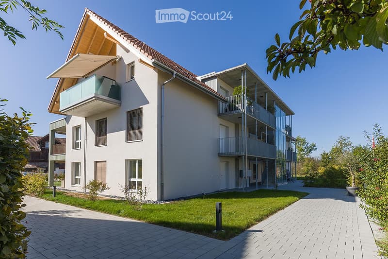 Modern two-story house with white exterior, multiple balconies, and a well-maintained lawn.