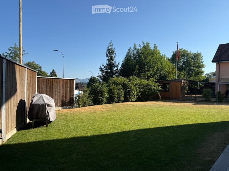 Well-maintained lawn with a covered grill, wooden fence, and trees in the background.