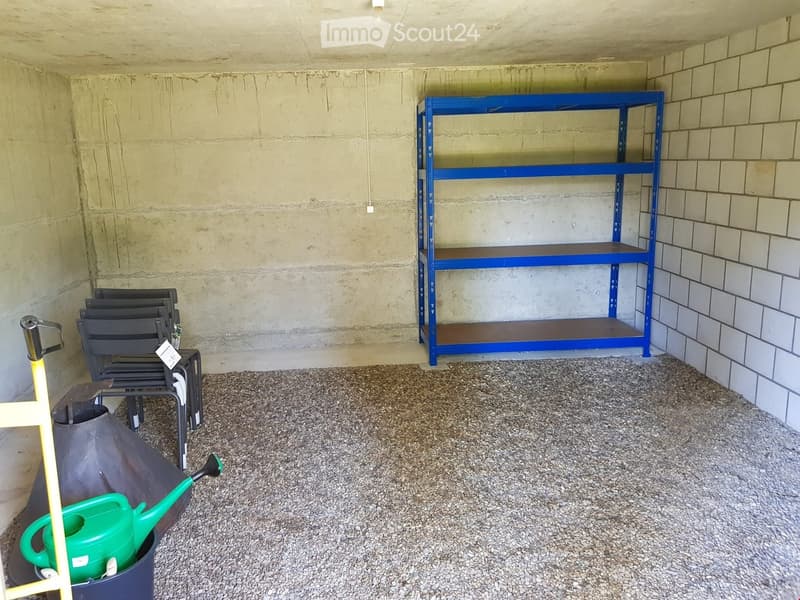 Garden shed with concrete walls, gravel floor, blue metal shelving unit, black chairs, and a green watering can.