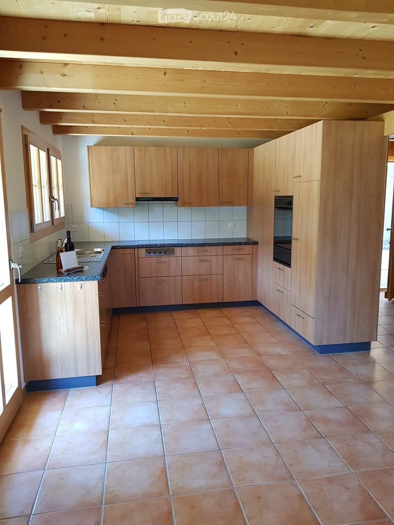 Modern kitchen with light wooden cabinets, granite countertop, stainless steel sink, and built-in oven. Exposed wooden beams on the ceiling and tiled floor.