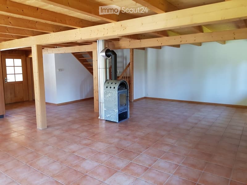 Empty room with exposed wooden beams, tiled floor, and a wood-burning stove with chimney. No furniture or furnishings present.