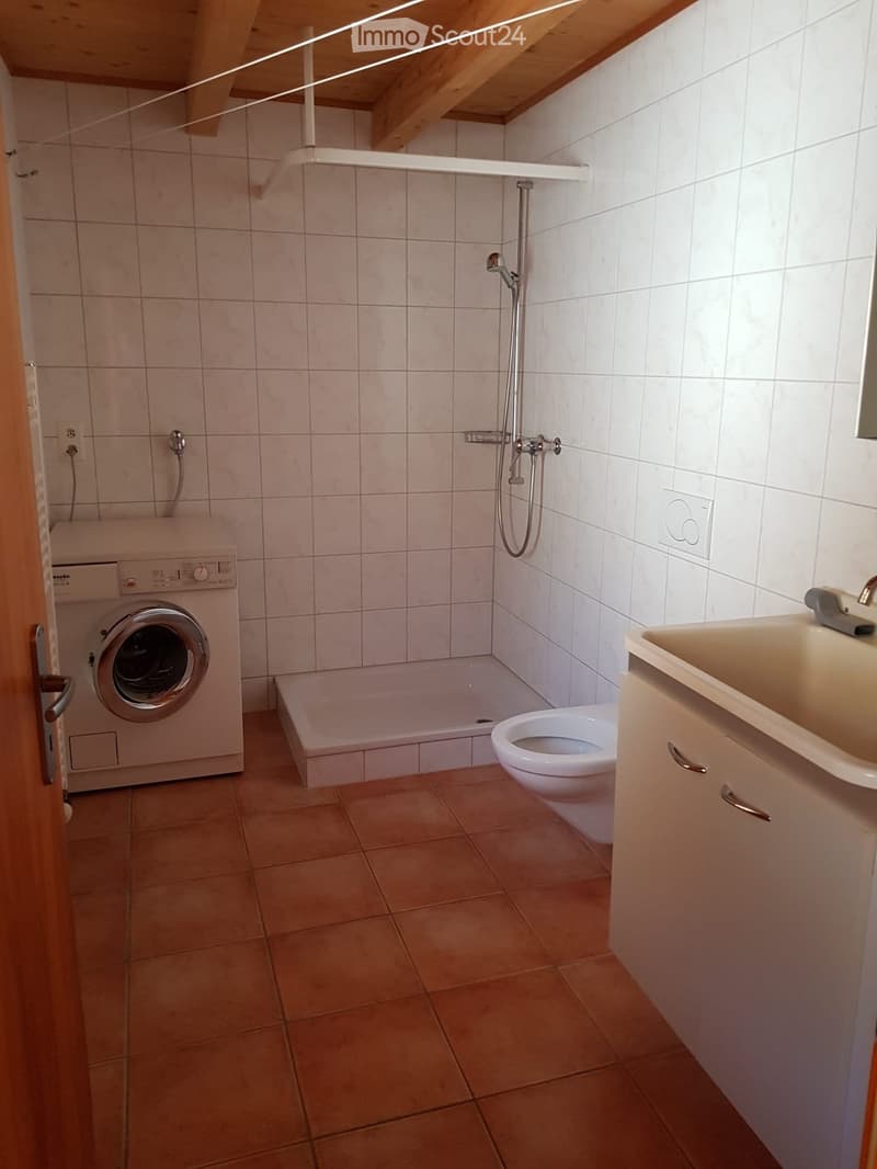 Bathroom with tiled walls and floor, featuring a bathtub, toilet, sink, washing machine, and shower fixture.