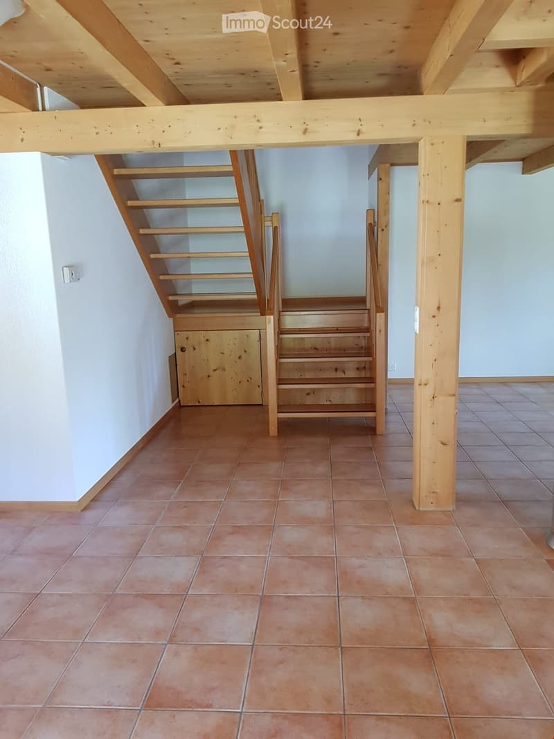 Empty hallway with wooden staircase, tiled floor, and exposed wooden beams on the ceiling.
