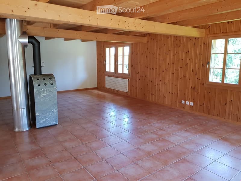 Empty room with wooden walls, tiled floor, exposed wooden beams, and a wood-burning stove with a chimney.