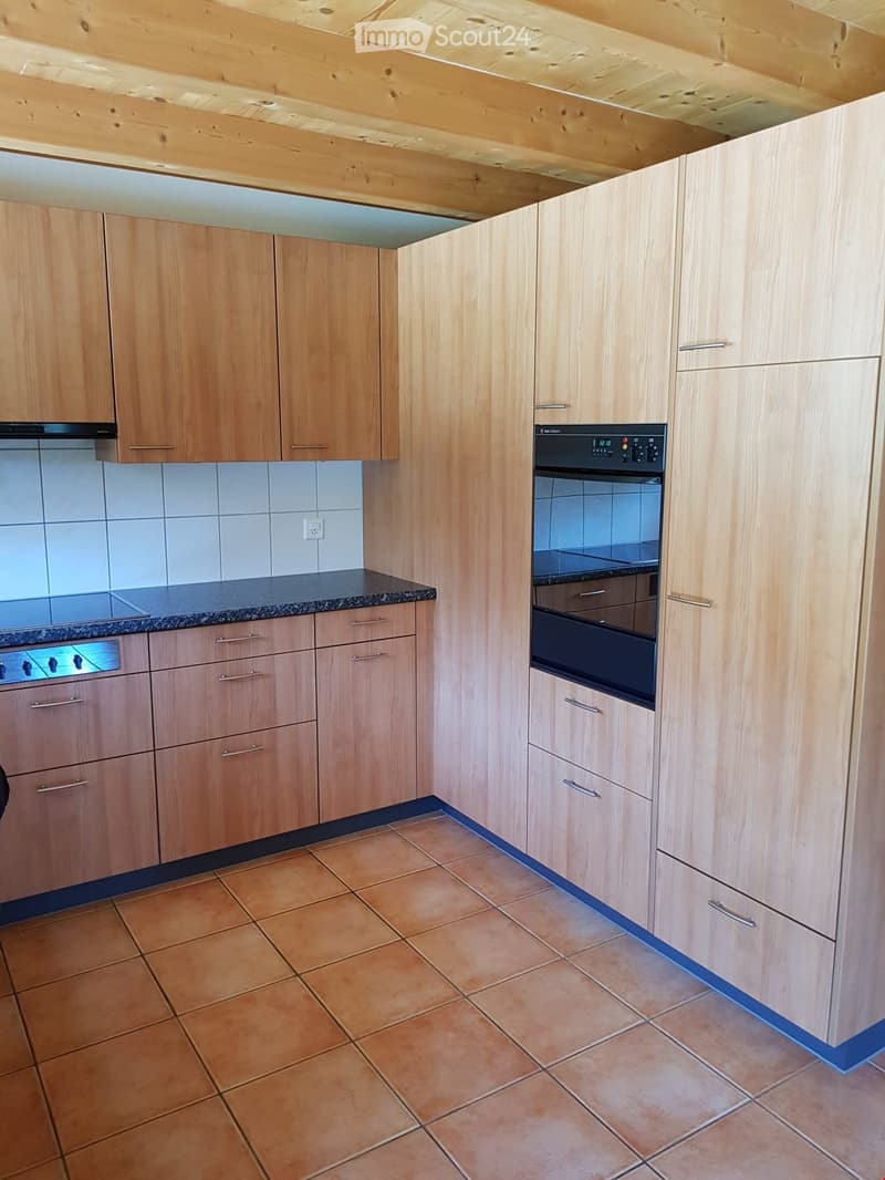 Modern kitchen with light wooden cabinets, granite countertop, and tiled floor.