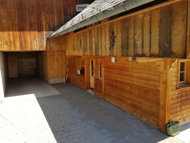 Wooden stable with a brick-paved area, broom, and a woven basket visible.