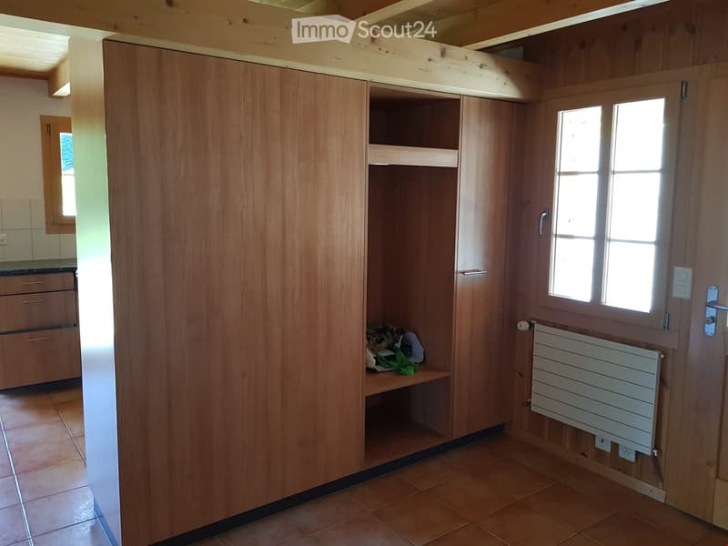 A small, well-lit room with wooden walls and tiled flooring, featuring a large wardrobe with shelves and a radiator on the wall.
