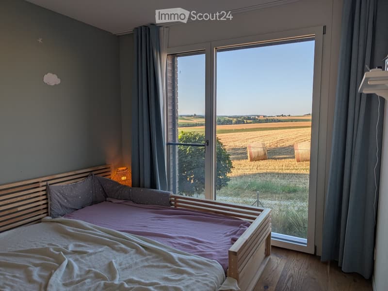Cozy bedroom with a wooden bed, soft bedding, and large windows offering a scenic rural view.