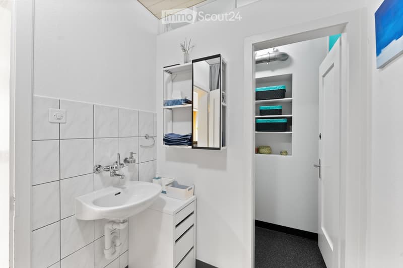 Modern bathroom with white tiles, a sink, a mirror cabinet, and a built-in storage cabinet with shelves and baskets.