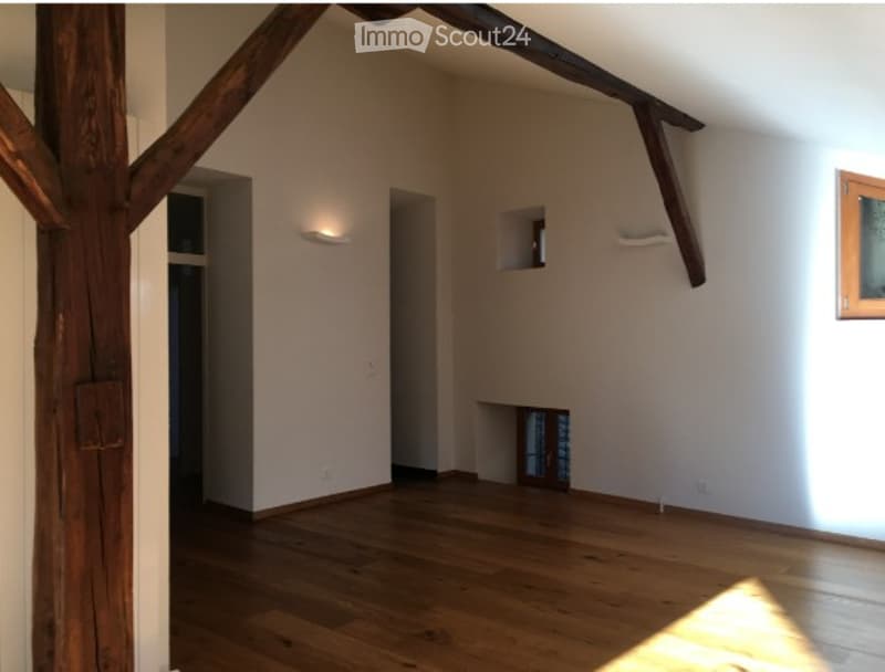 Empty room with wooden floor, exposed wooden beams, white walls, and a small built-in shelf.