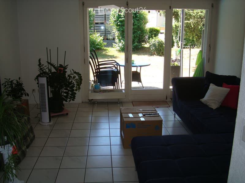 Living room with tiled floor, large sliding glass doors opening to a patio, sofa, coffee table, fan, and plants.