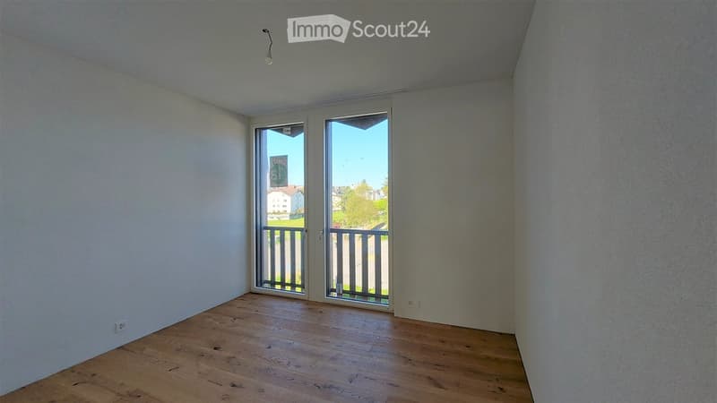 Empty room with wooden flooring, white walls, and large glass doors leading to a balcony.