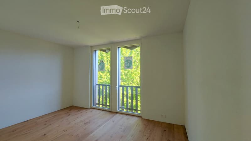 Empty room with wooden flooring, white walls, and large sliding glass doors leading to a balcony.