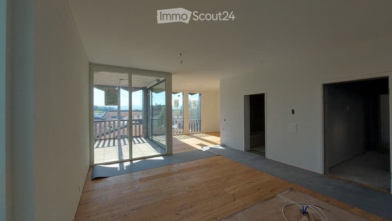 Empty room with wooden flooring, large glass sliding doors leading to a balcony, and neutral-colored walls.
