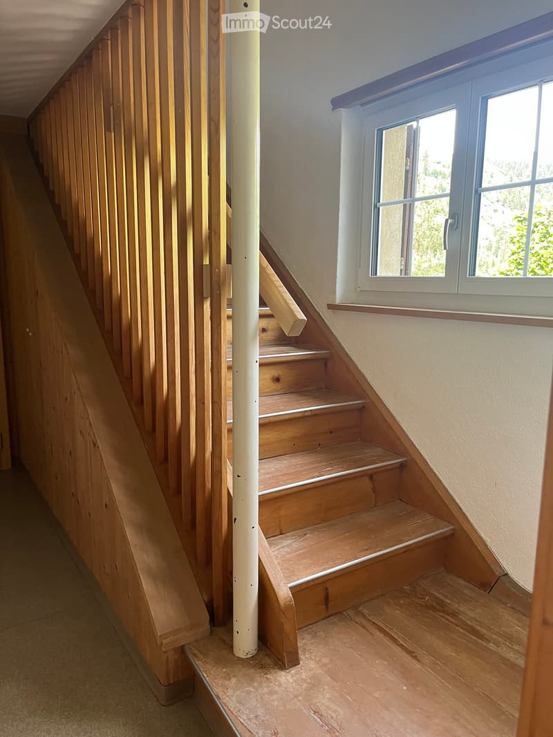 Wooden staircase with vertical slatted railing, white painted wall, and a window with white frame and glass panes.