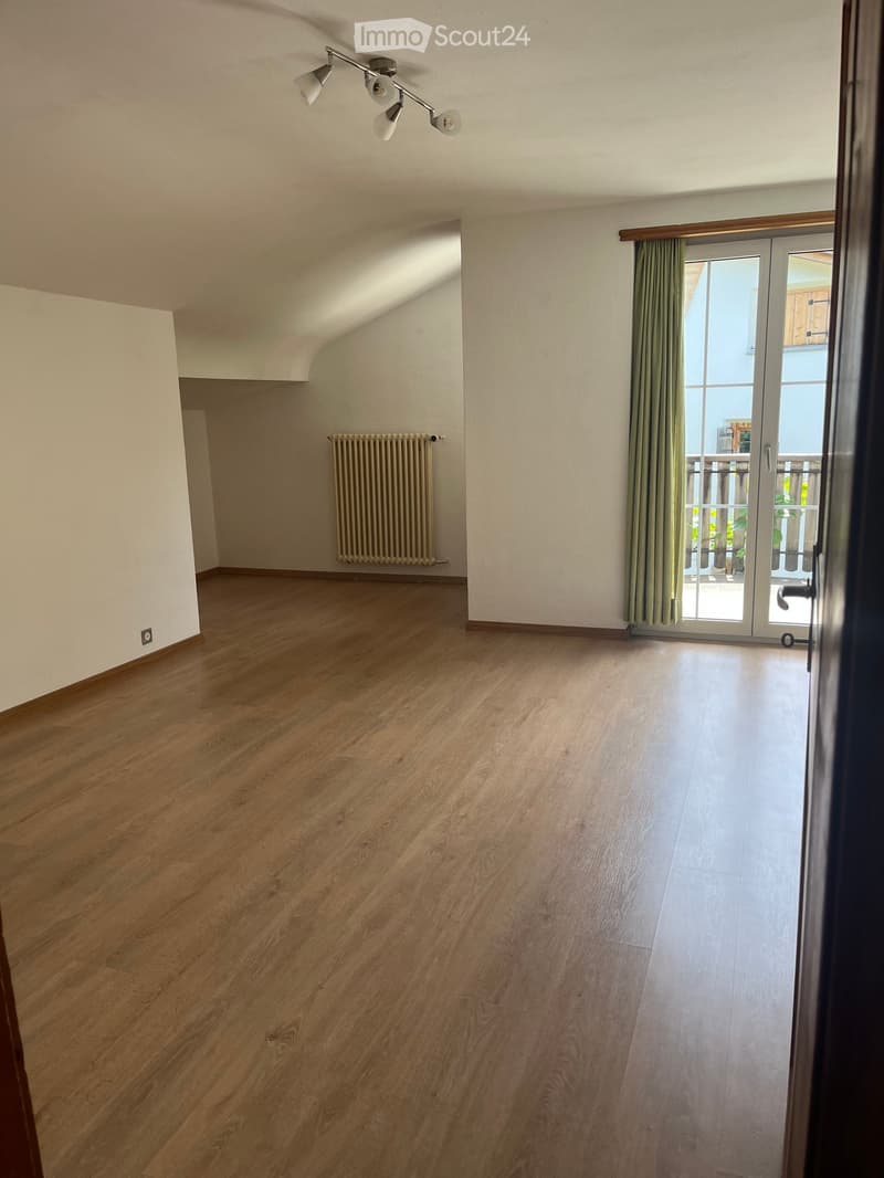 Empty room with wooden flooring, white walls, a radiator, and a sliding glass door leading to a balcony.