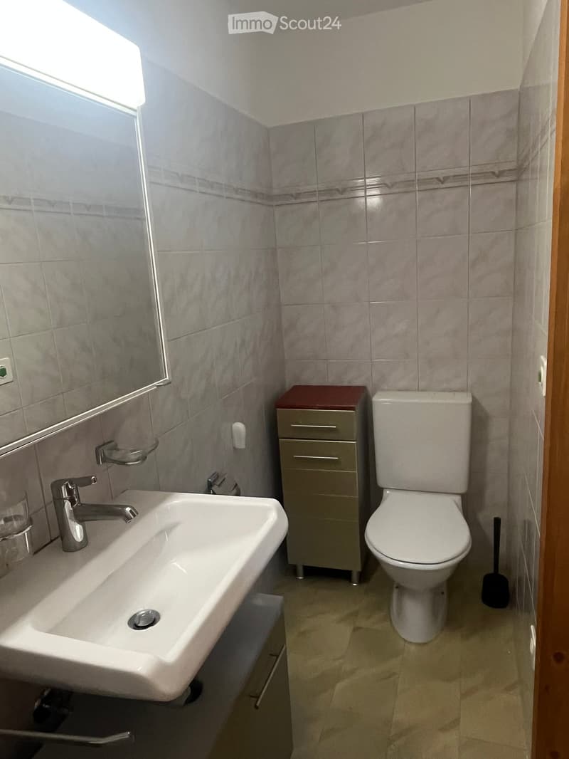 Modern bathroom with a white sink, chrome faucet, mirror, toilet, and a small cabinet with drawers.