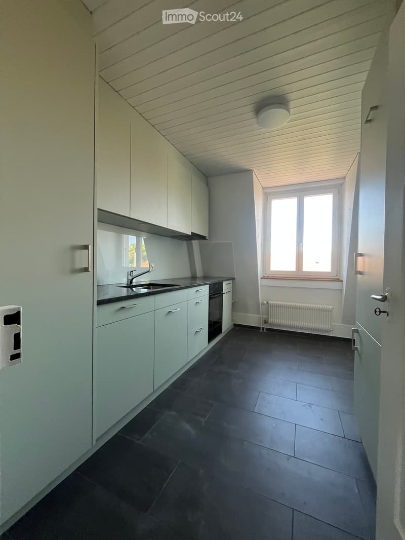 Modern kitchen with white cabinets, dark tiled floor, sink, faucet, and oven. Large window provides natural light.