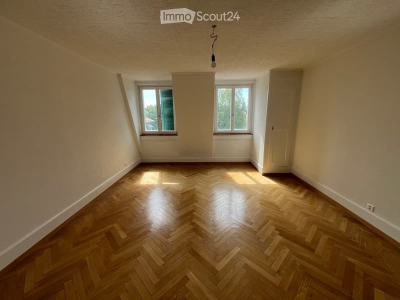 Empty room with wooden herringbone flooring, two windows, and a door. No furniture or equipment present.