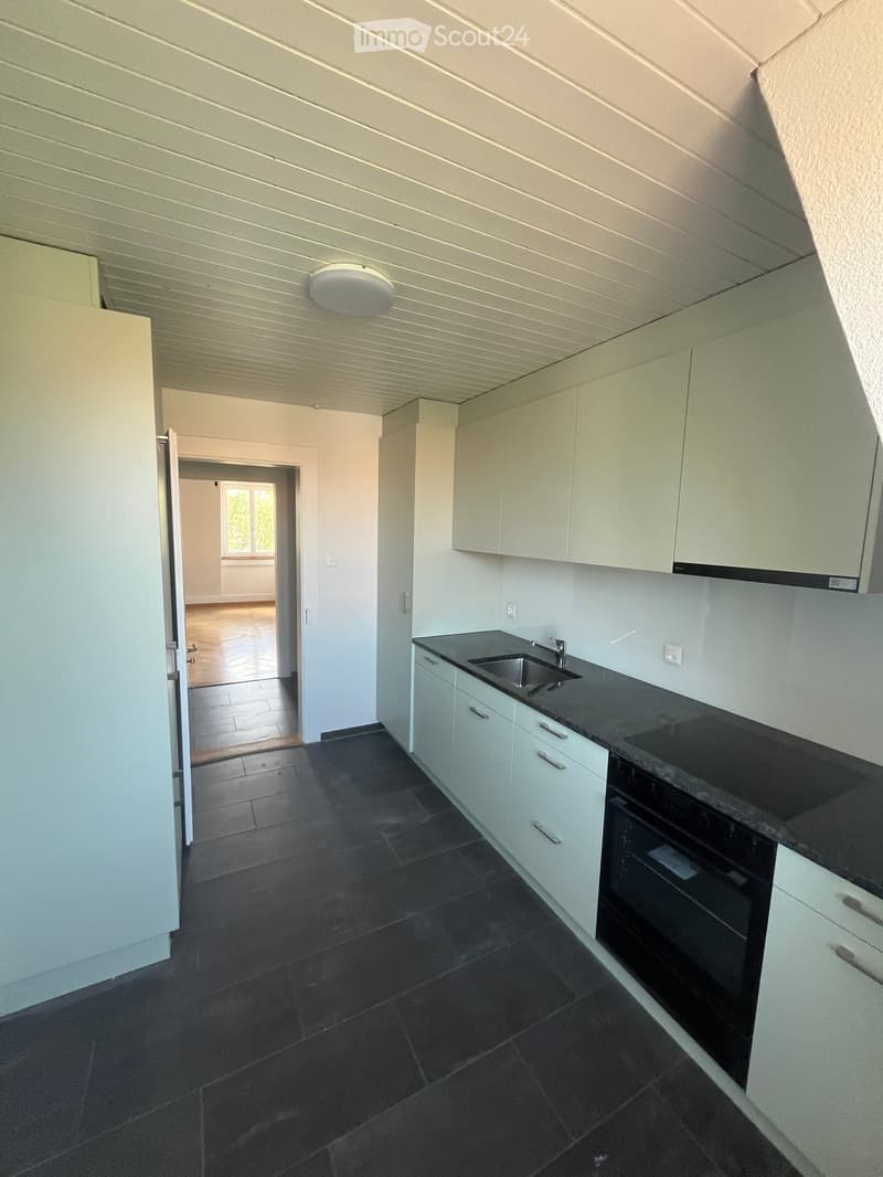 Modern kitchen with white cabinets, black countertops, and dark tiled flooring. Features a sink, oven, and built-in cabinets.